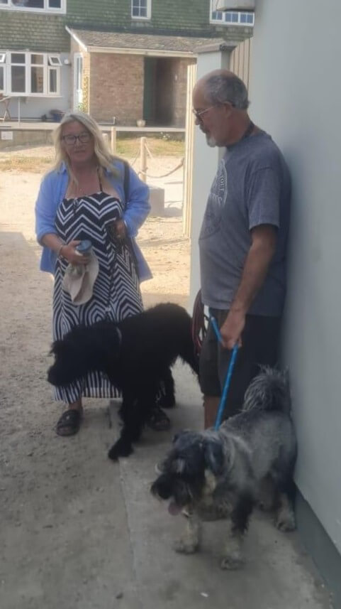 A man and a woman standing with two dogs outside a building