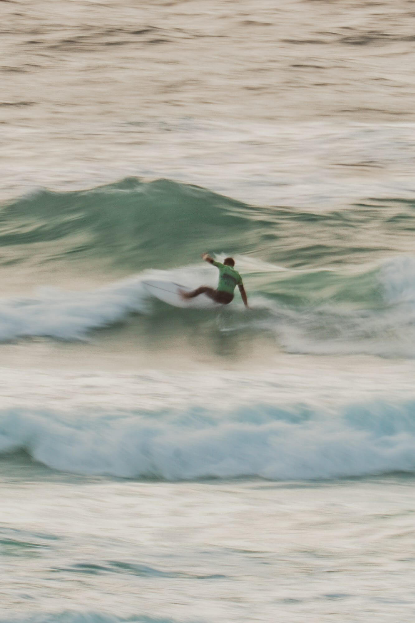 A panned action shot of a surfer in a green jersey powering along a wave at Fistral