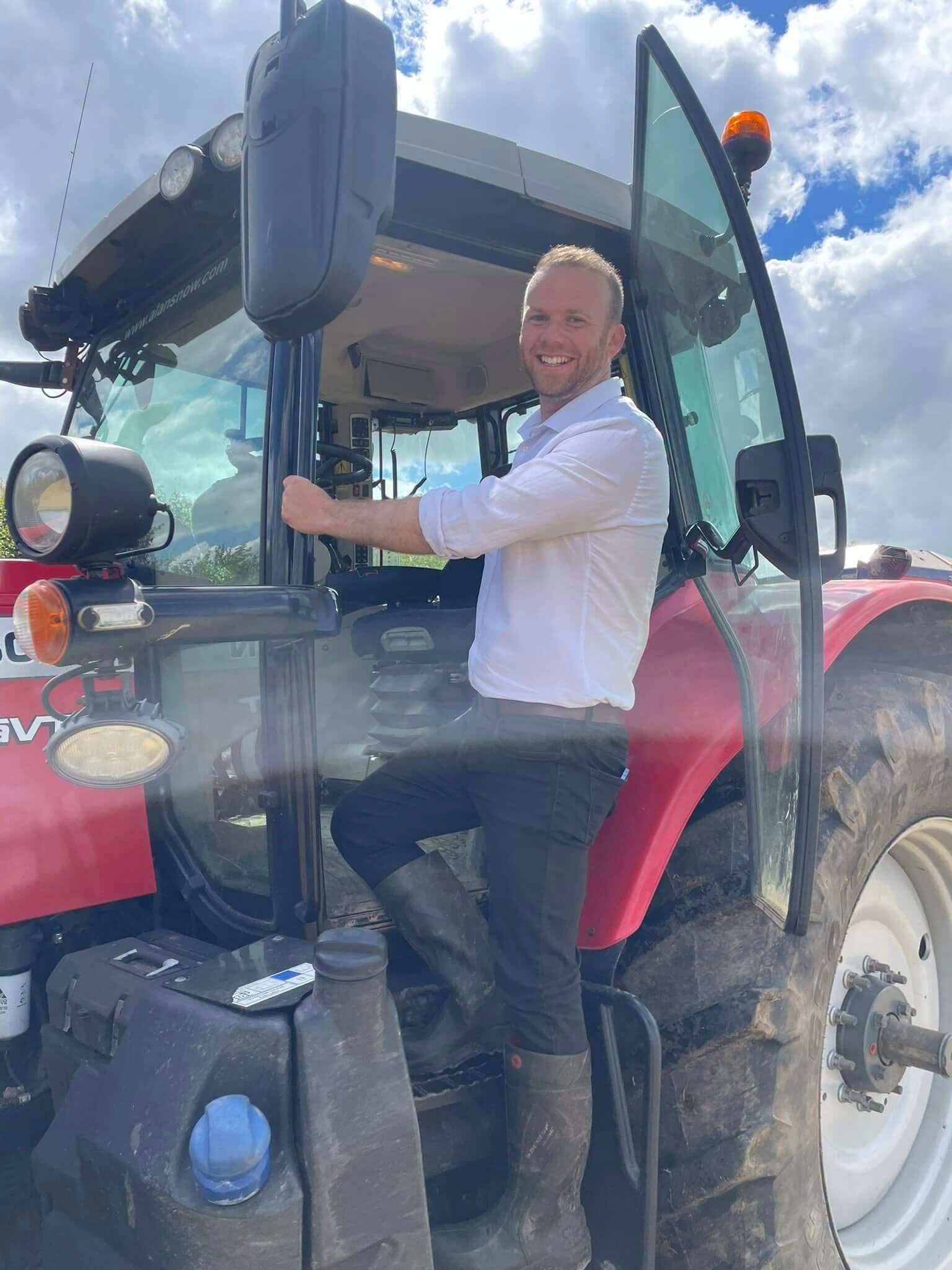 North Cornwall MP Ben Maguire smiling on the step of a red tractor