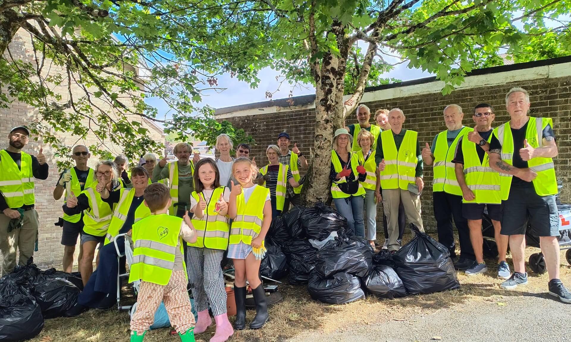 Volunteers in hi-vis vests stand under a tree beside piles of black bin bags after a Bodmin litter pick