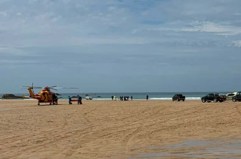 Emergency vehicles and a rescue helicopter on Porthcothan beach beside the sea