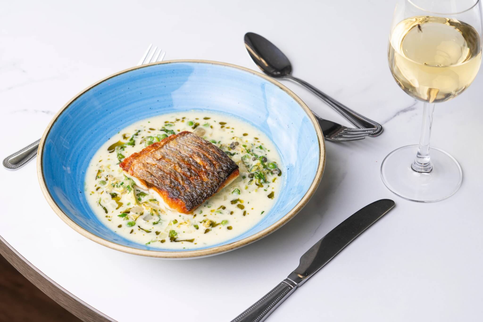 Pan-fried sea bass fillet in a creamy pea and herb broth
