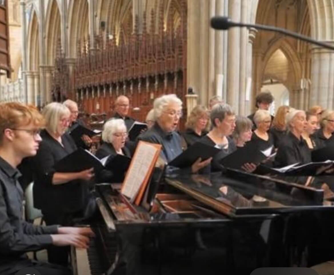 Members of the choir singing from black folders beside a grand piano