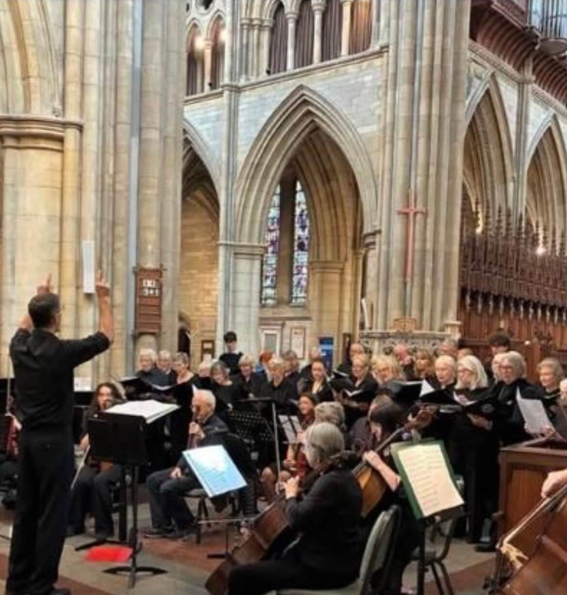 A choir and orchestra performing under the arches of Truro Cathedral, conducted from the left