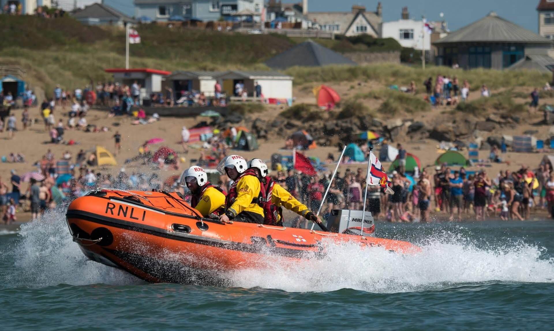 Bude RNLI inshore lifeboat crew powering past a packed beach during Lifeboat Weekend