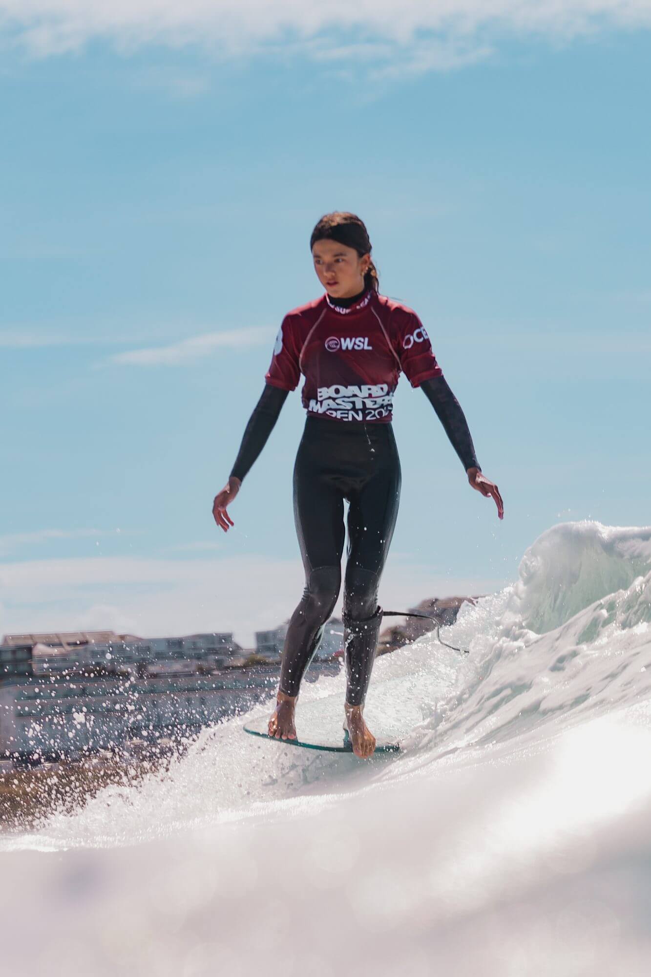 A competitor in a maroon WSL Boardmasters Open jersey walks the nose of her board on a wave at Fistral