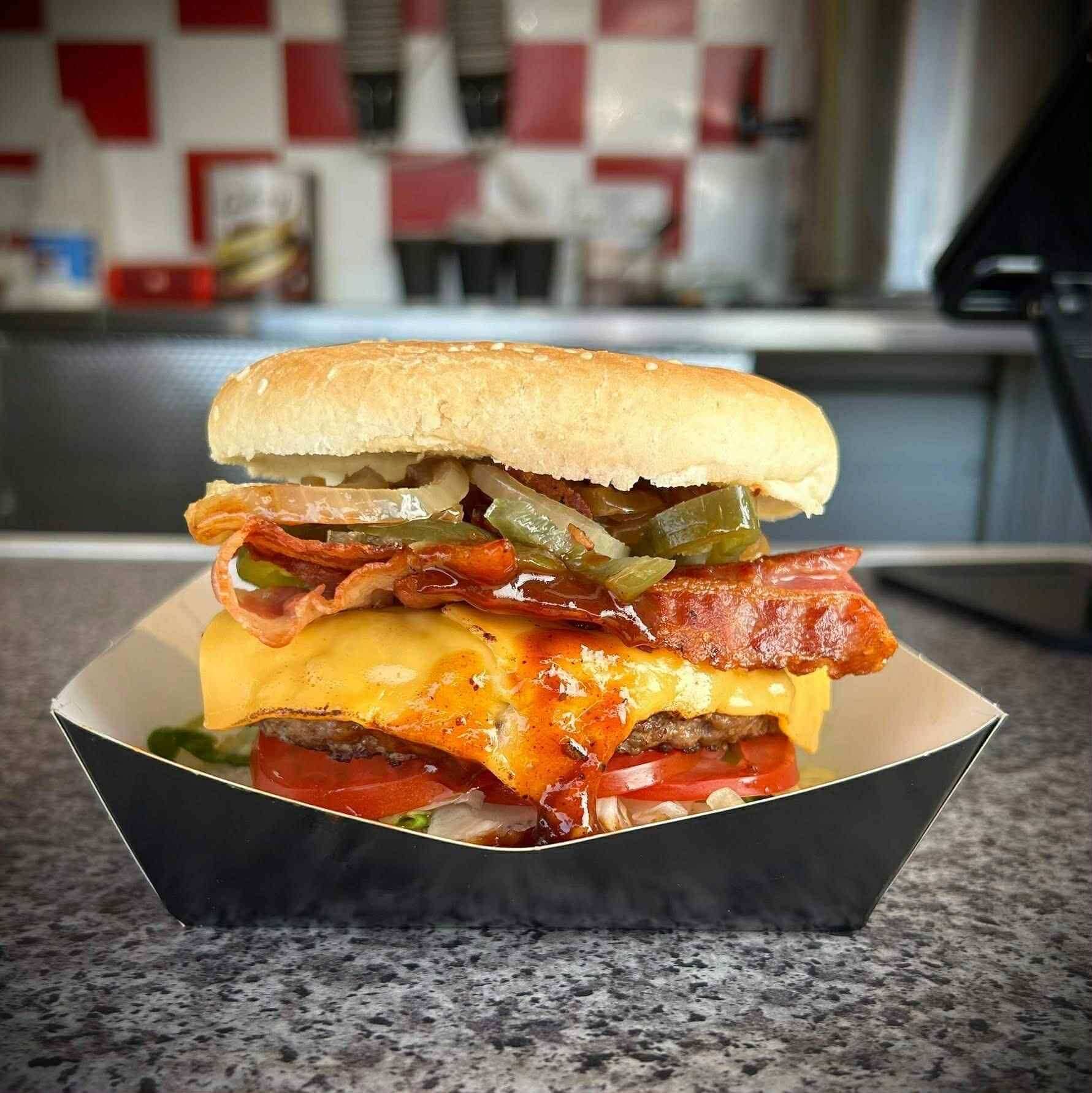 A loaded cheeseburger with bacon and peppers in a tray at Xander's Diner