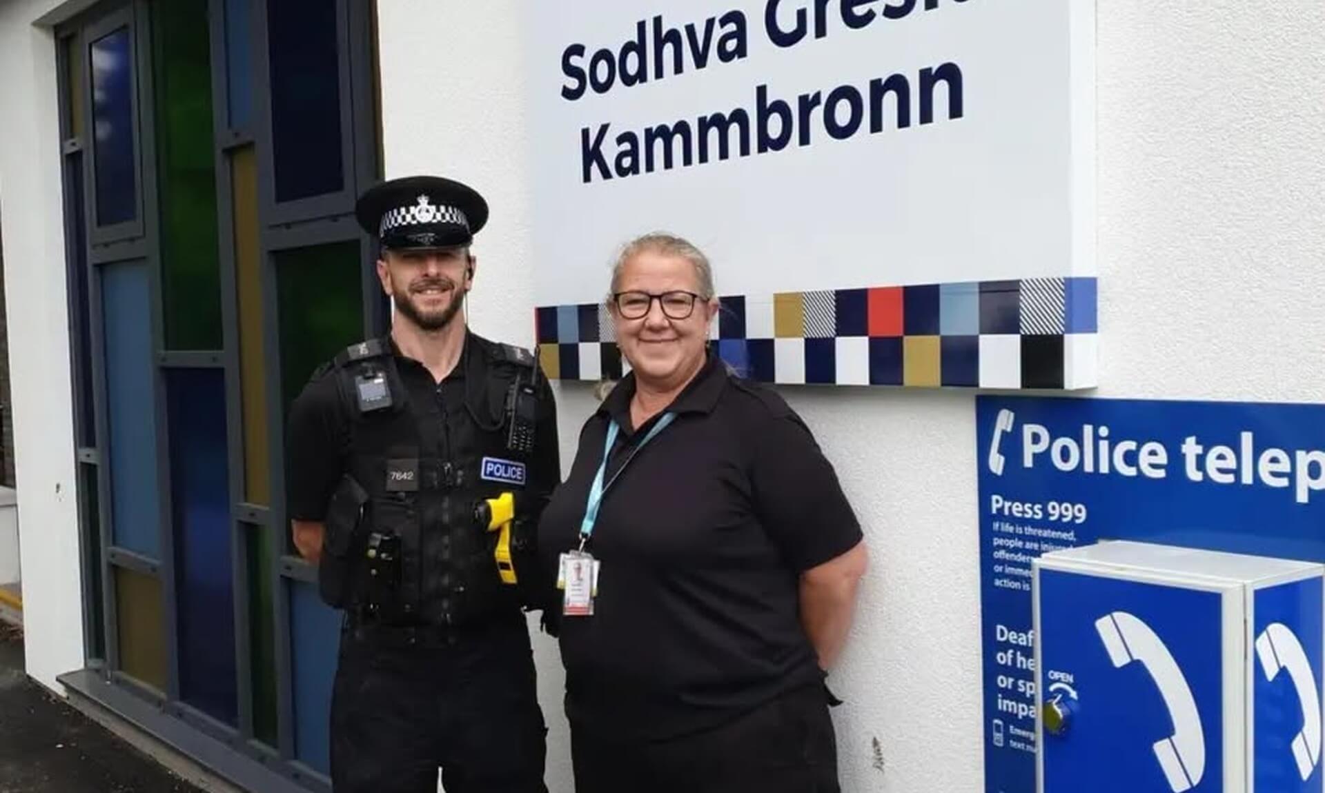 A police officer and a PCSO stand smiling outside Camborne Police Station beneath the bilingual English and Cornish sign