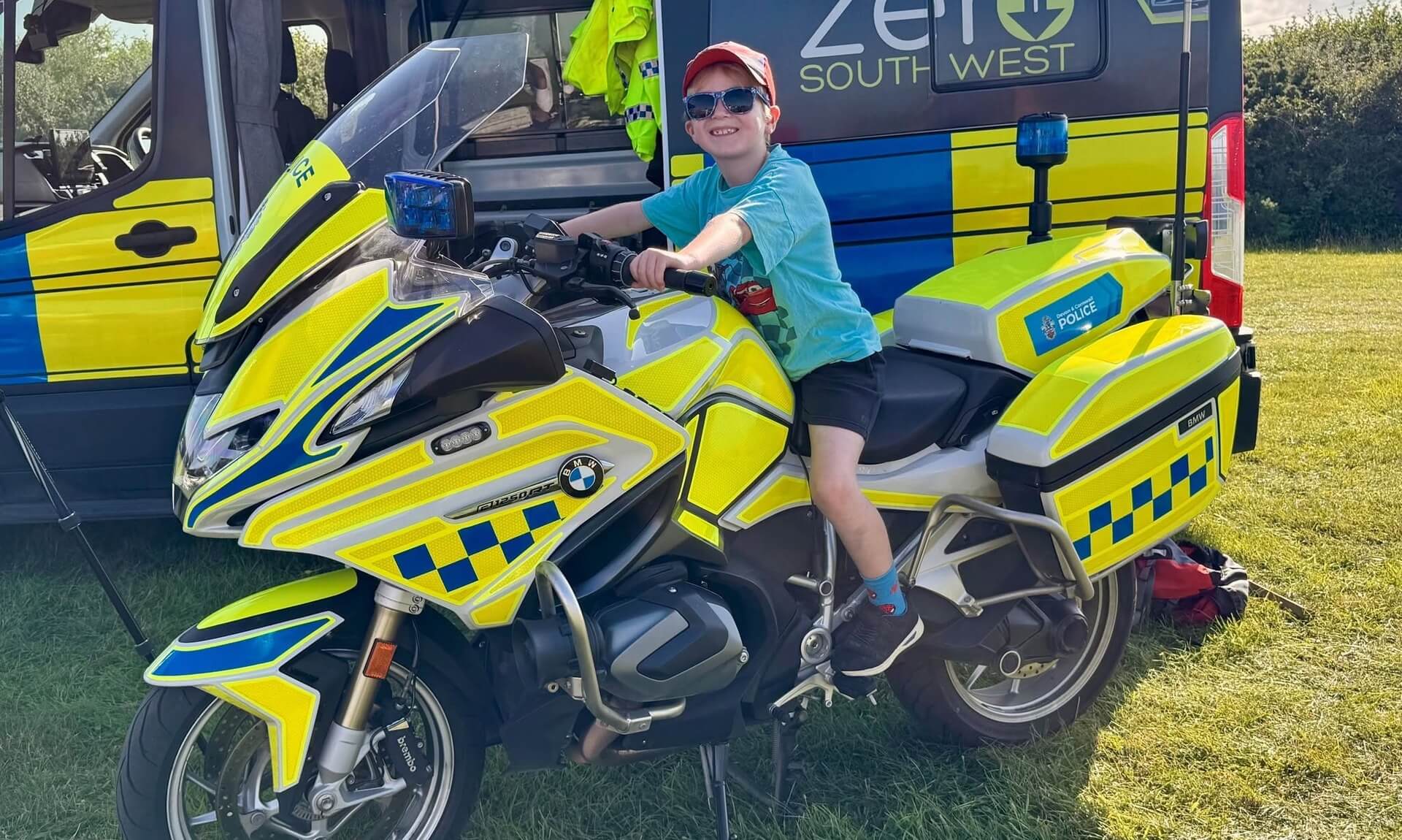 A boy in sunglasses and a red cap sits on a Devon and Cornwall Police BMW motorcycle at the Camelford Show