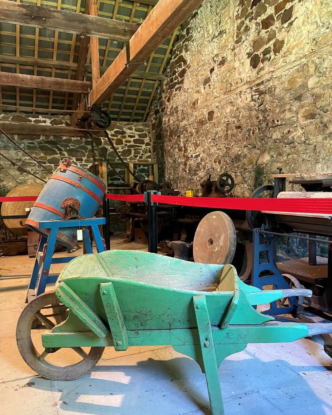 A restored wheelbarrow and workshop machinery on display at Helebridge