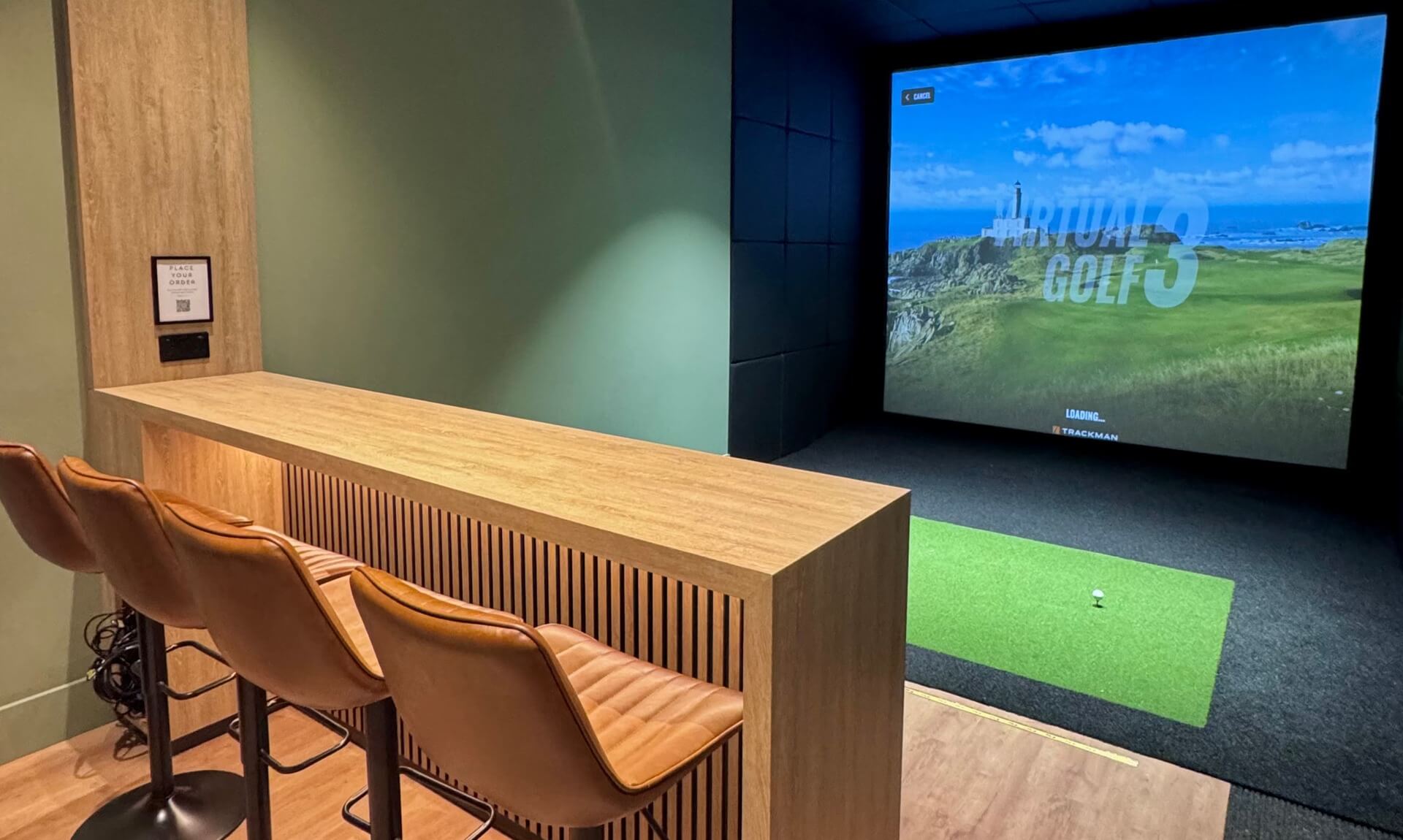 The new TrackMan golf simulator studio at Carlyon Bay Golf Club, with bar seating, a screen showing a coastal course and a putting mat