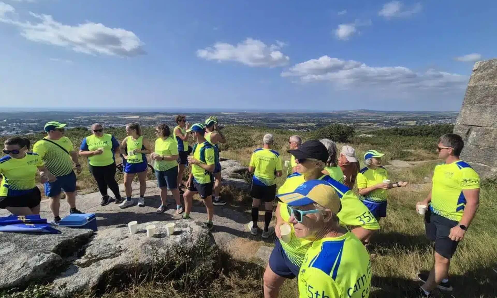 Carn Runners members in club kit gathered on the summit of Carn Brea with views across Camborne and Redruth