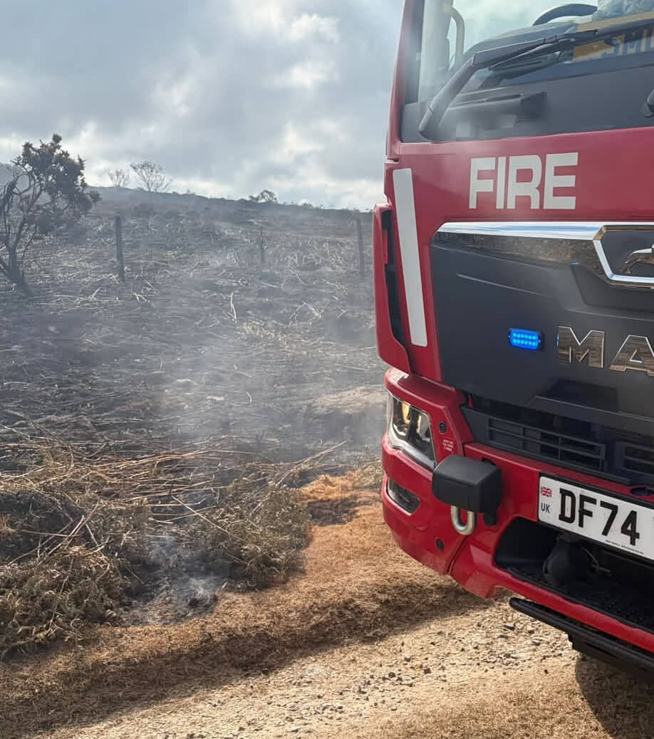 Fire engine on a track beside burnt ground still smouldering after the Chapel Carn Brea wildfire