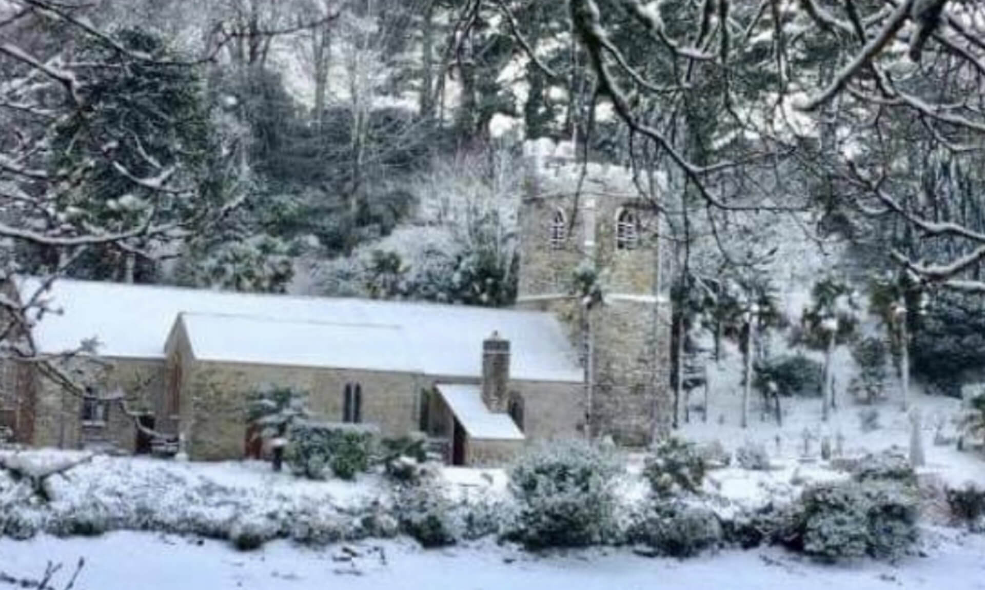 St Just in Roseland church under snow, seen across a frozen creek through snow-covered branches