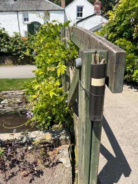 A black stick holder strapped to the Wisteria Bridge post, filled with sticks ready for a game of Pooh sticks