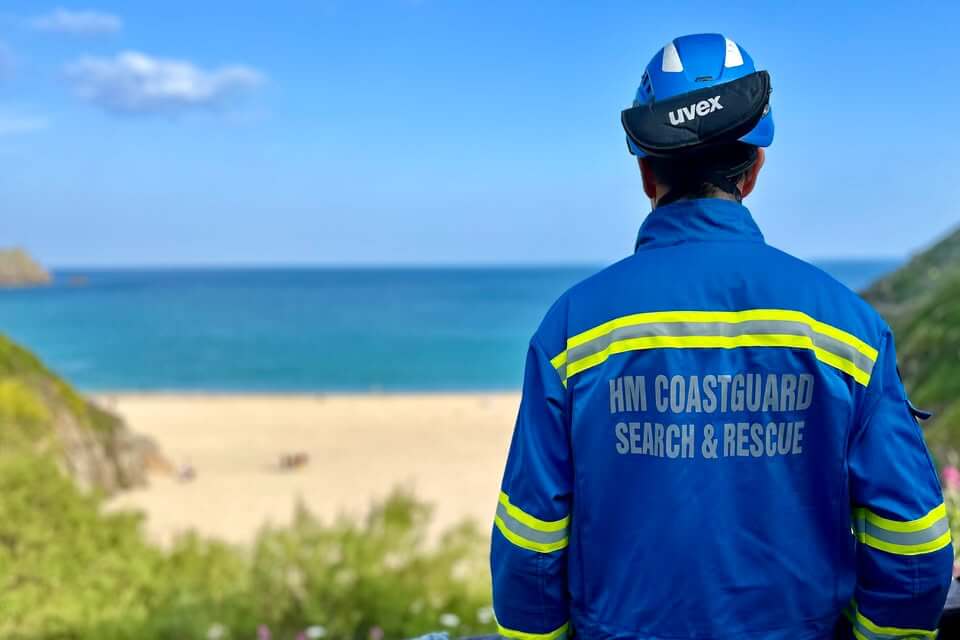 A Land's End Coastguard Rescue Team member on the cliff above Porthcurno beach on a sunny day