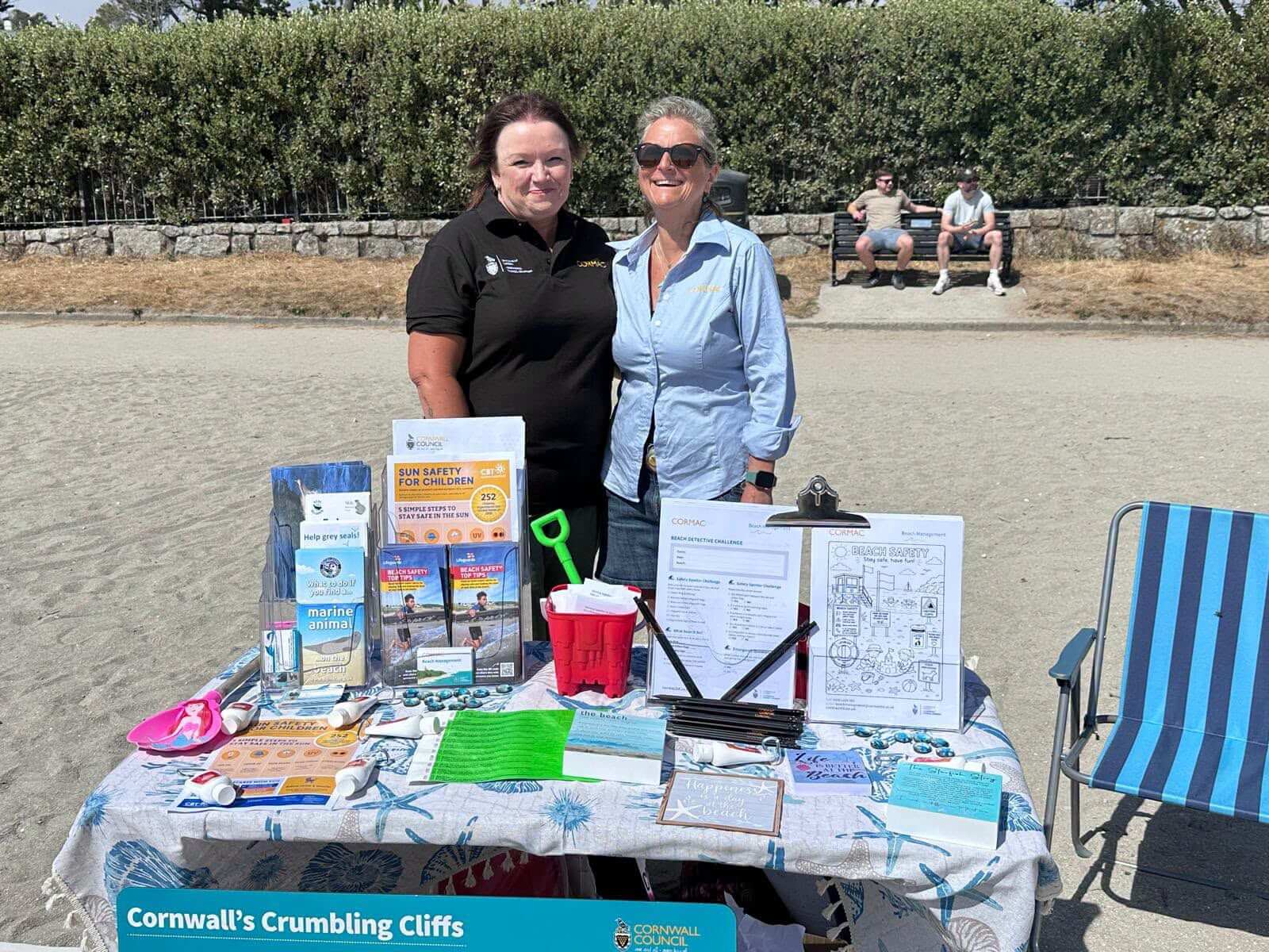 Two Cormac Beach Management staff standing behind their information stand on Gyllyngvase Beach