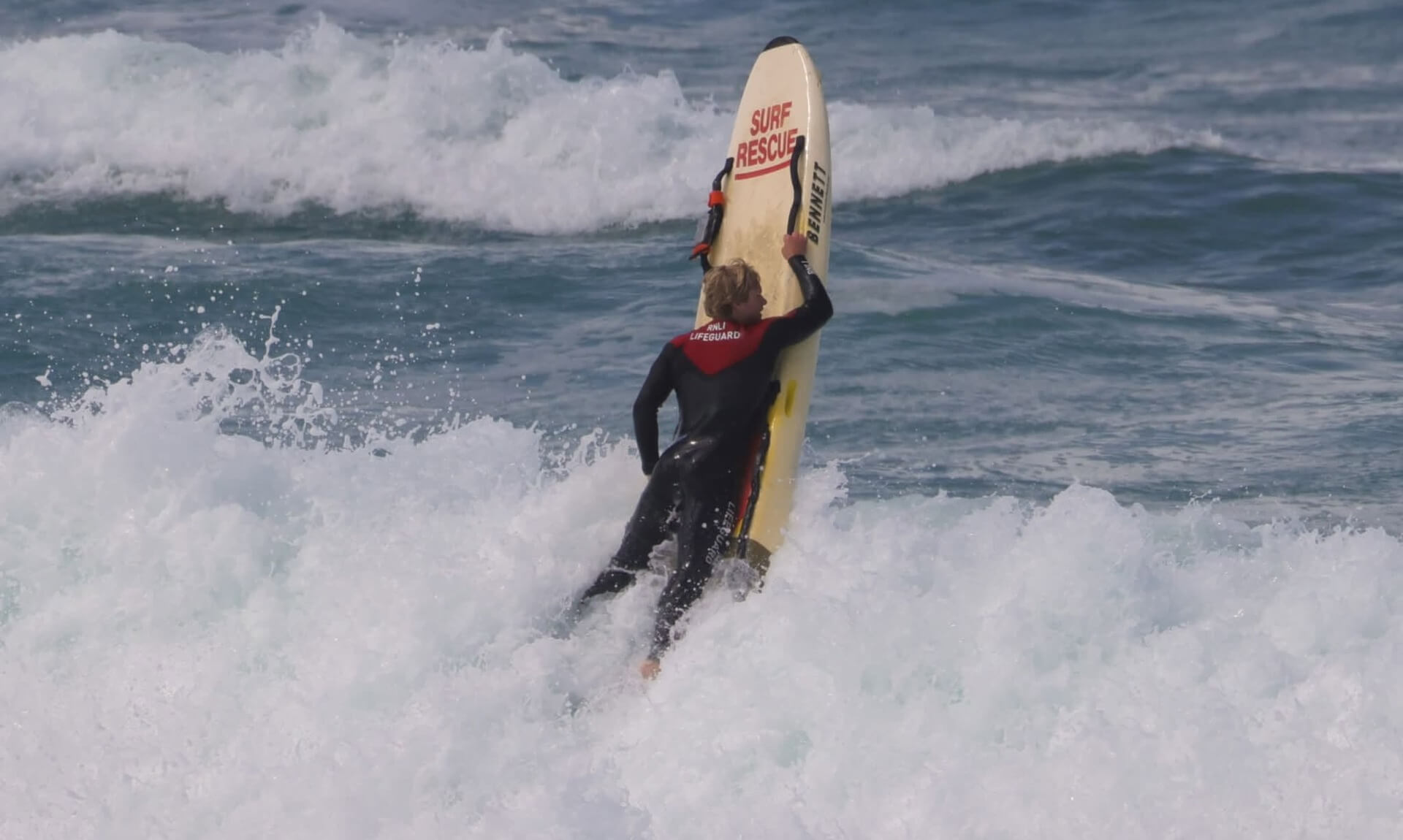 RNLI lifeguard carrying a surf rescue board through breaking waves
