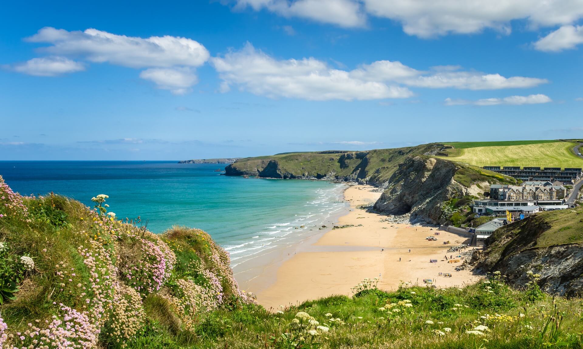 A sandy Cornish beach with turquoise sea and green cliffs on a sunny summer day