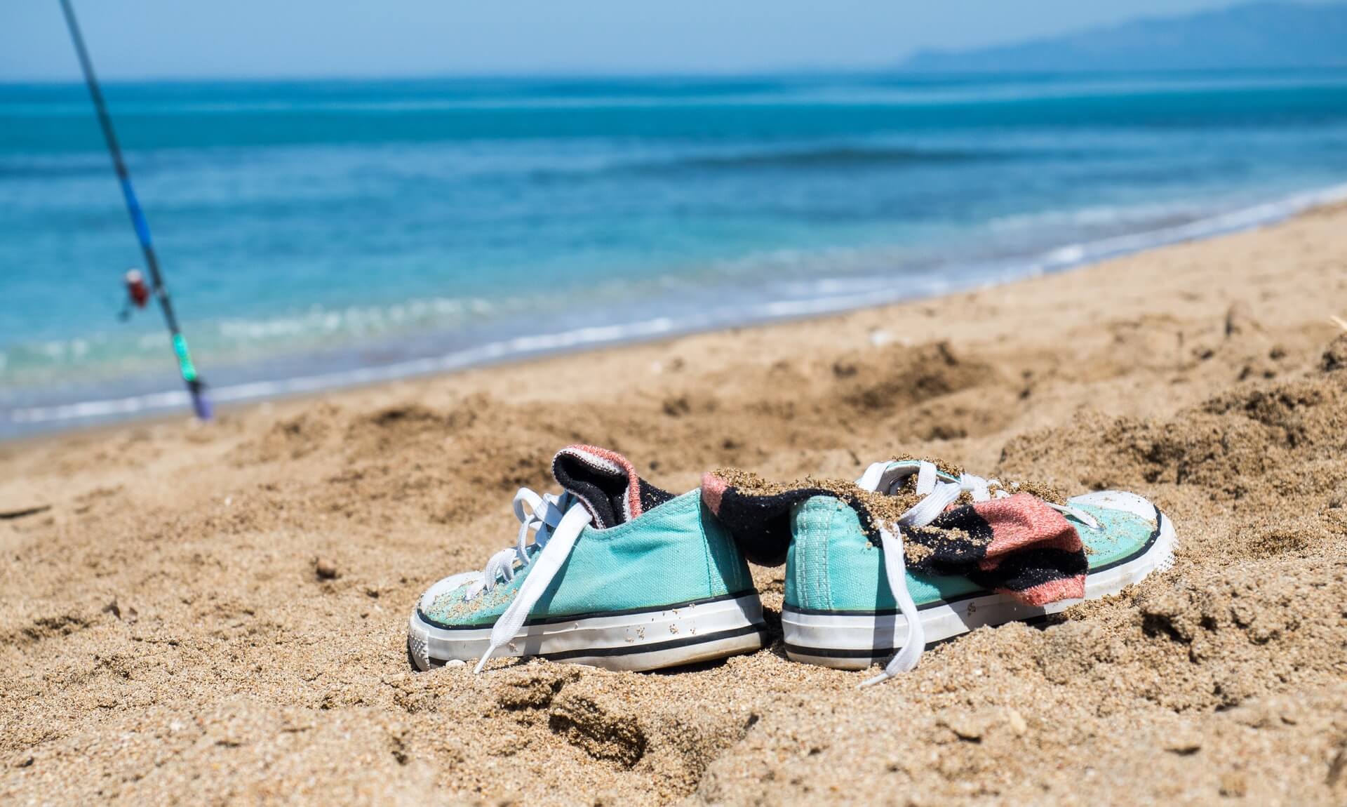 Sandy trainers and a discarded sock left behind on a beach with the sea in the background