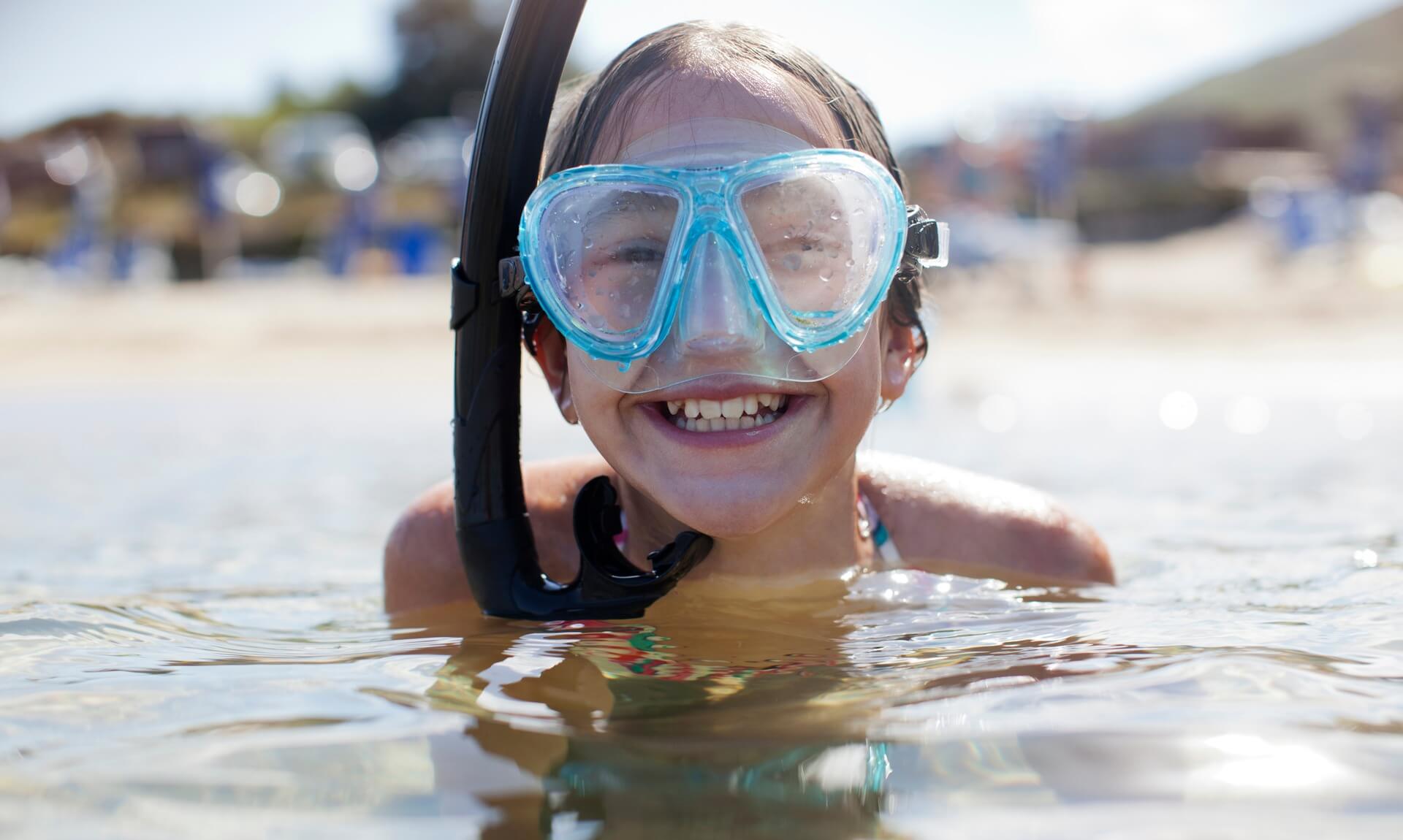 A smiling child in a snorkel mask in the sea on a sunny Cornwall beach