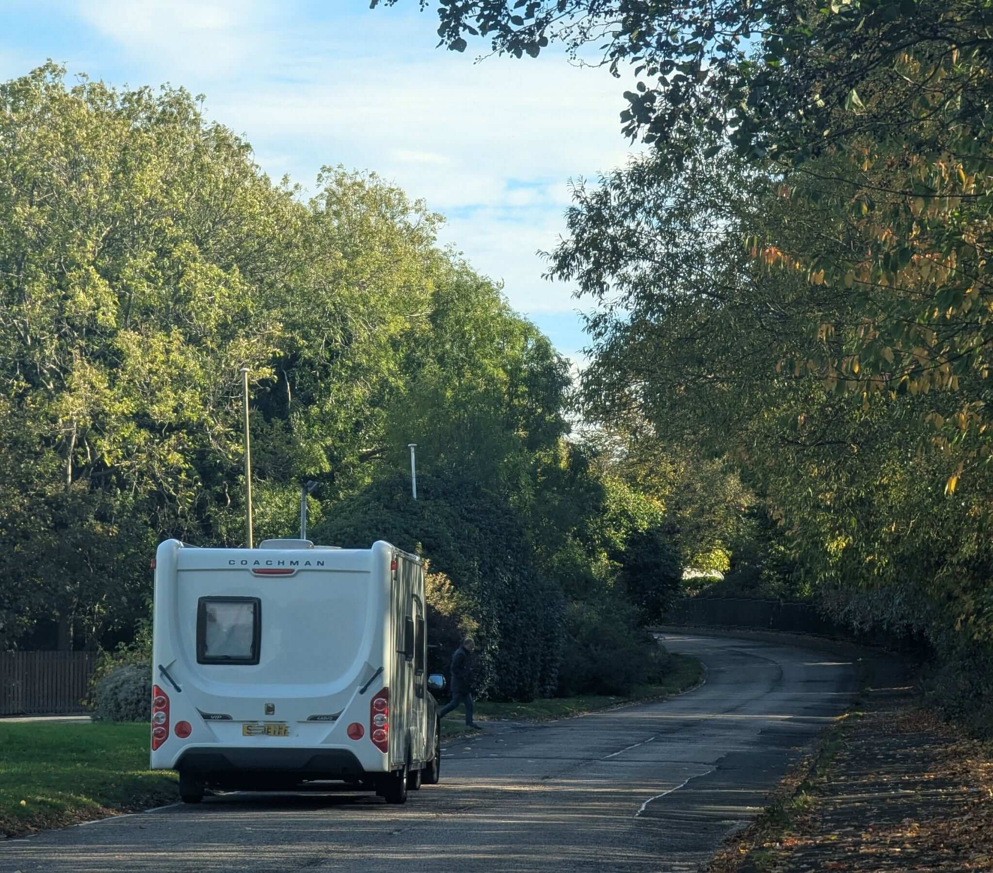 A white Coachman caravan being towed along a tree-lined road