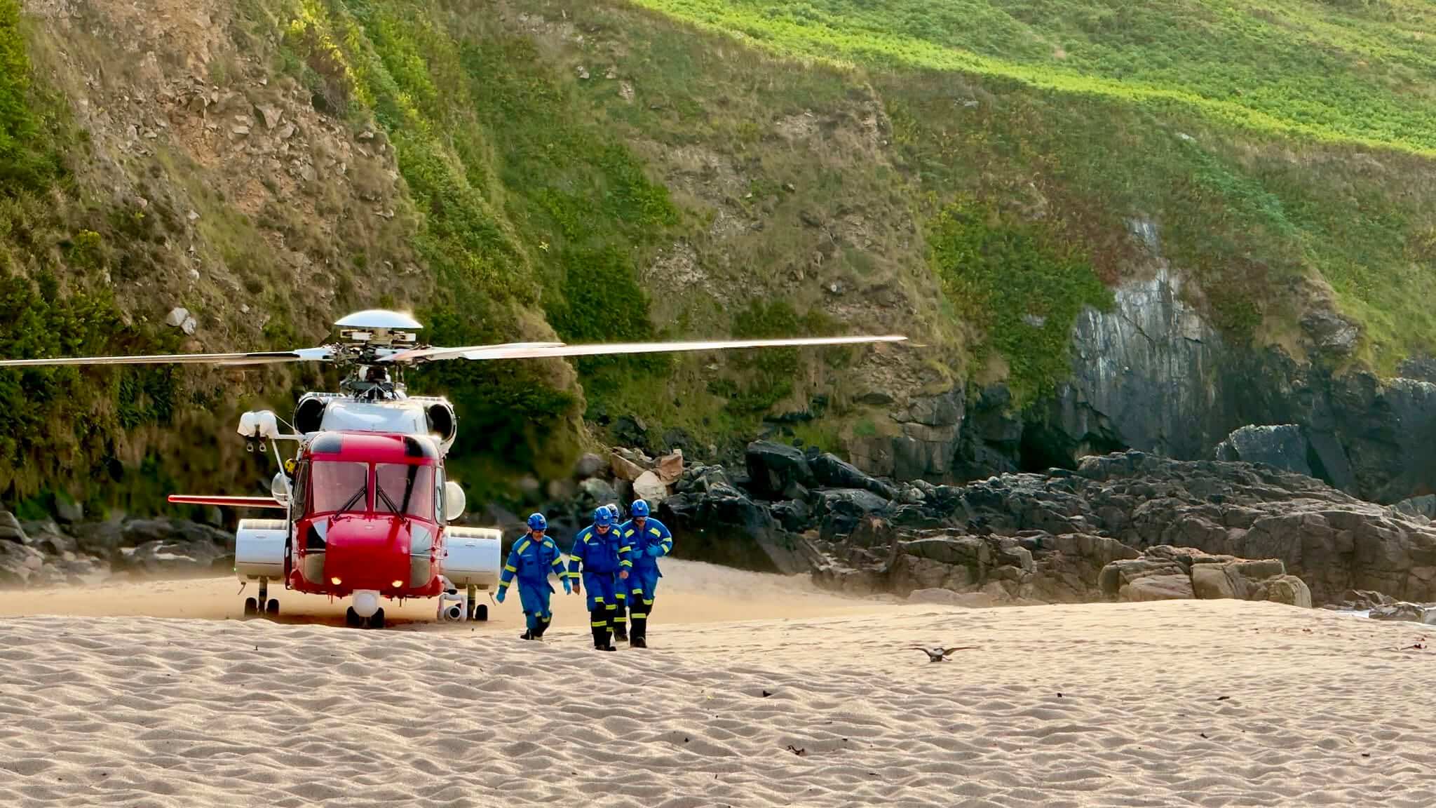 HM Coastguard helicopter landed on a Cornish beach with crew walking towards camera