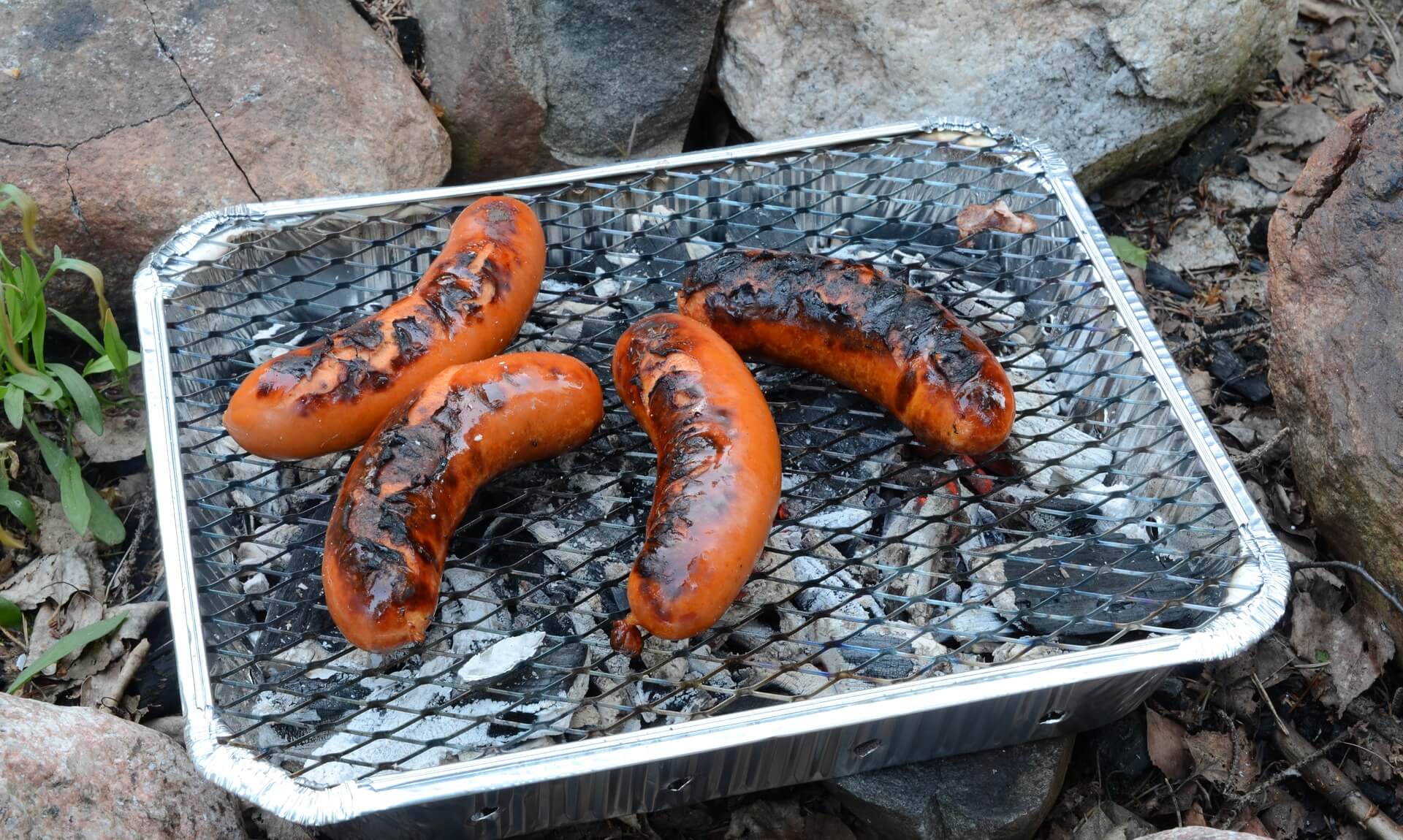 Sausages cooking on a disposable barbecue outdoors
