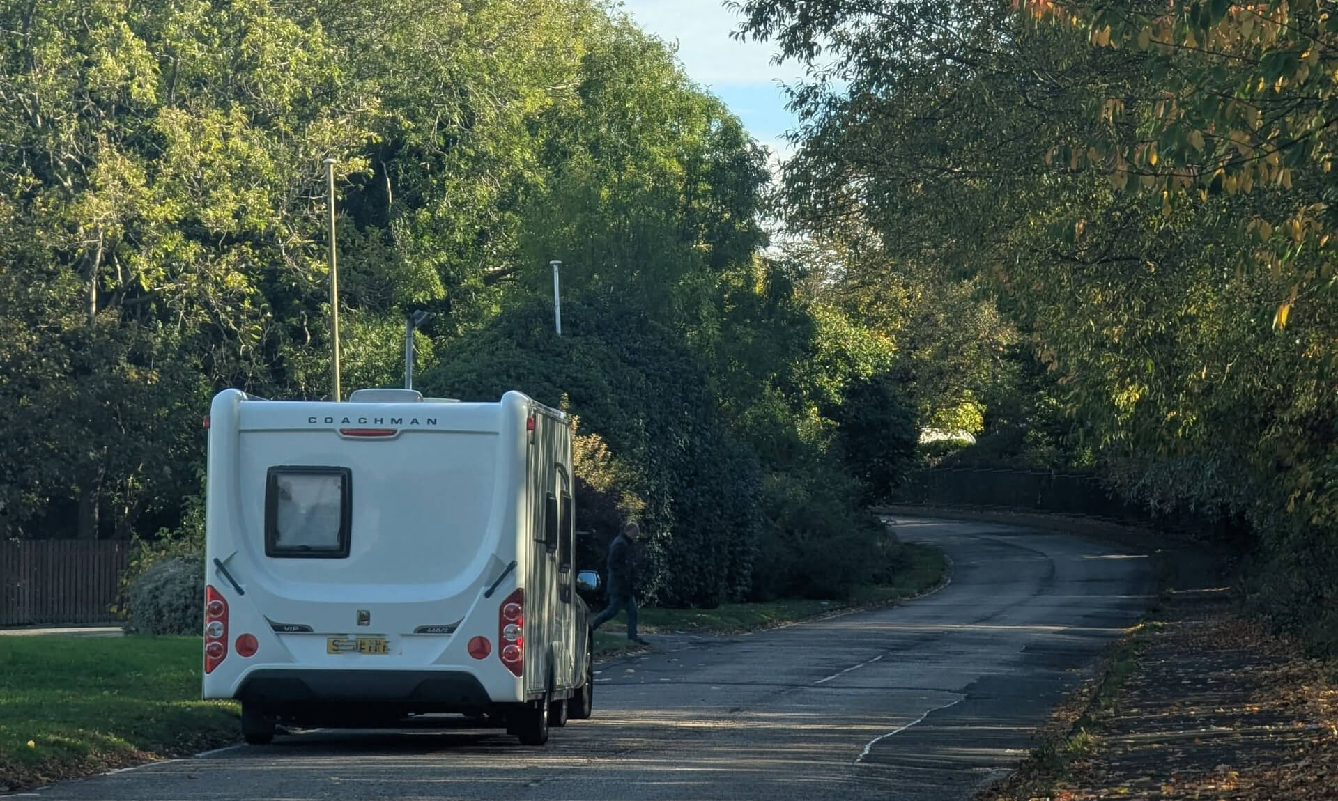 A white Coachman caravan being towed along a tree-lined road