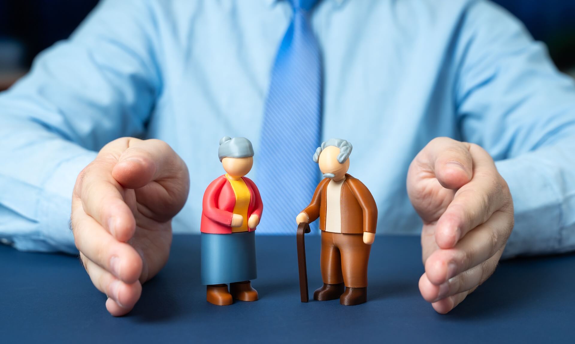 Hands held protectively either side of two small figurines of an elderly couple