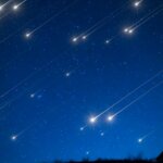 Bright meteors streaking across a dark blue night sky above a silhouetted horizon