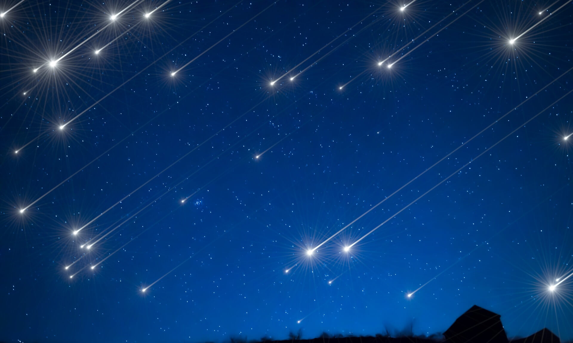 Bright meteors streaking across a dark blue night sky above a silhouetted horizon