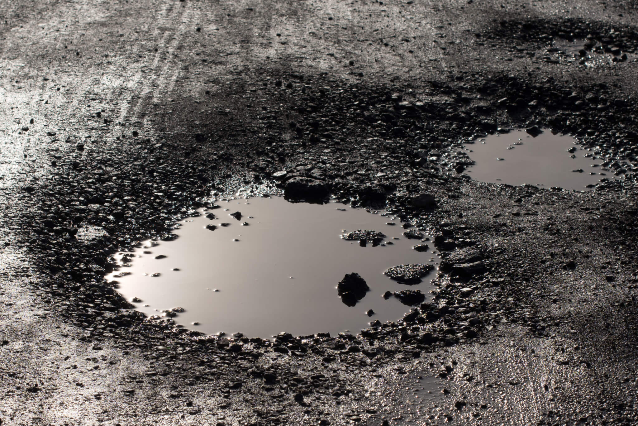 A large water-filled pothole in a dark tarmac road