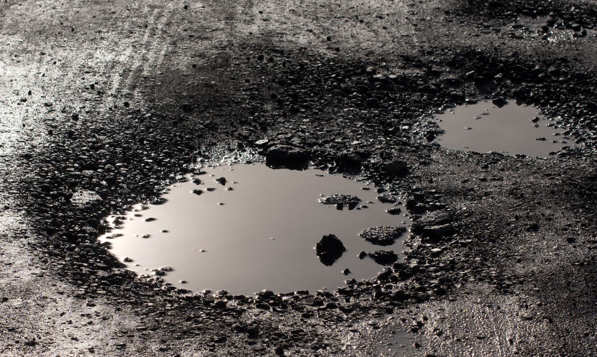 A large water-filled pothole in a dark tarmac road