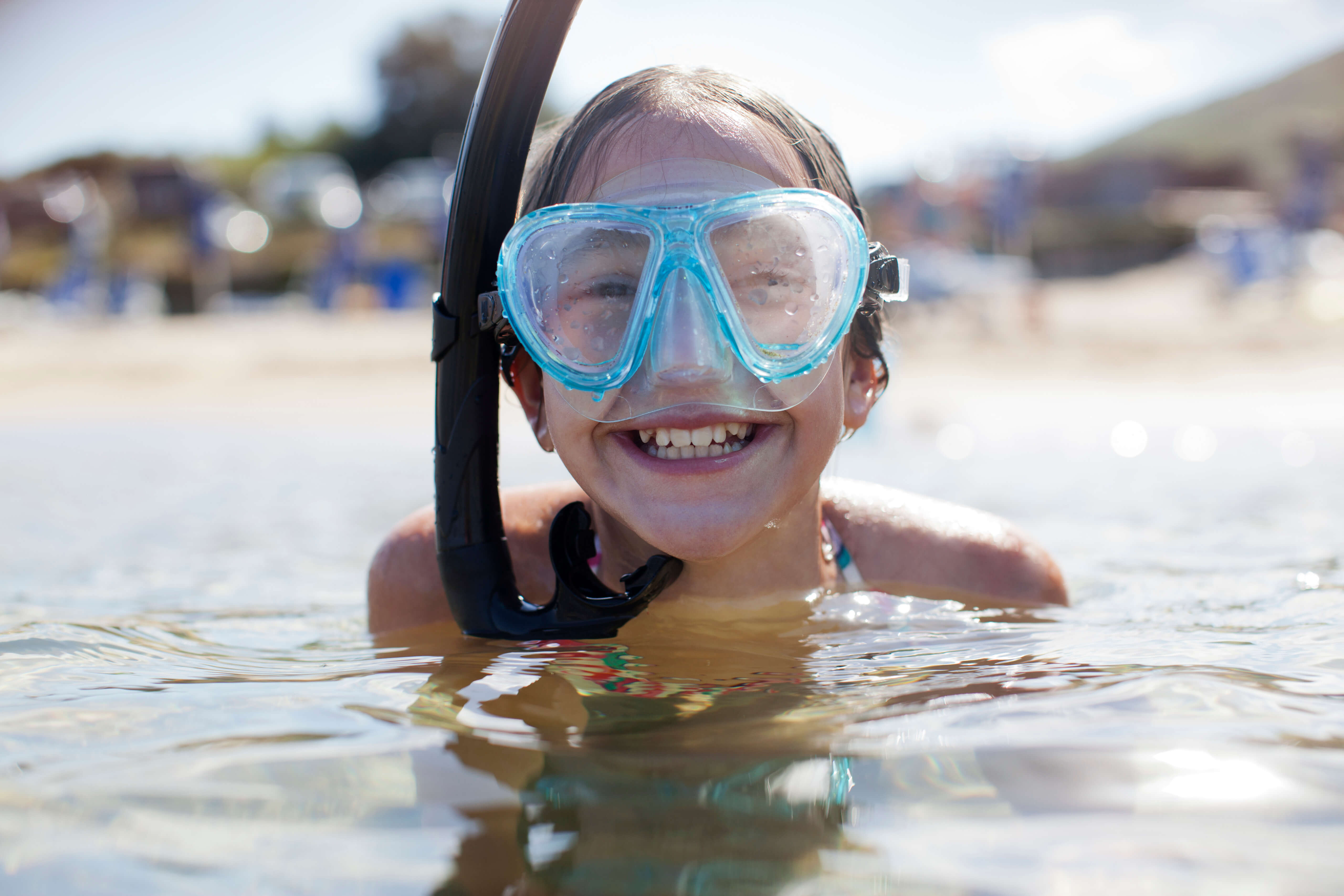A smiling child in a snorkel mask in the sea on a sunny Cornwall beach