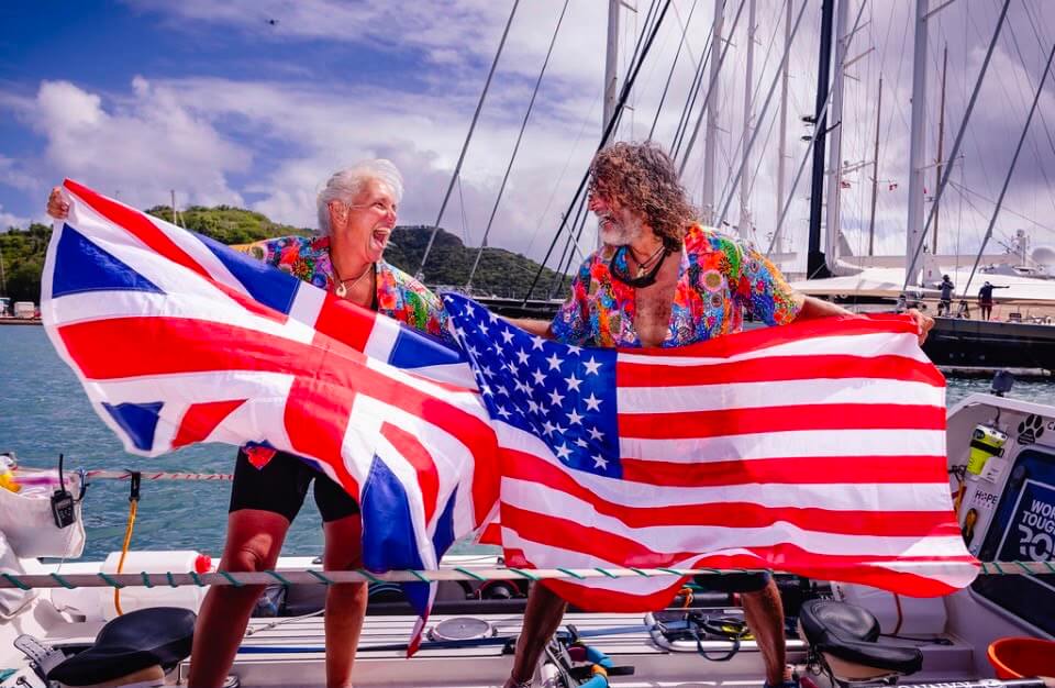 Dawn Smith and Paul Lore laughing on deck holding the Union flag and the US flag after an Atlantic crossing