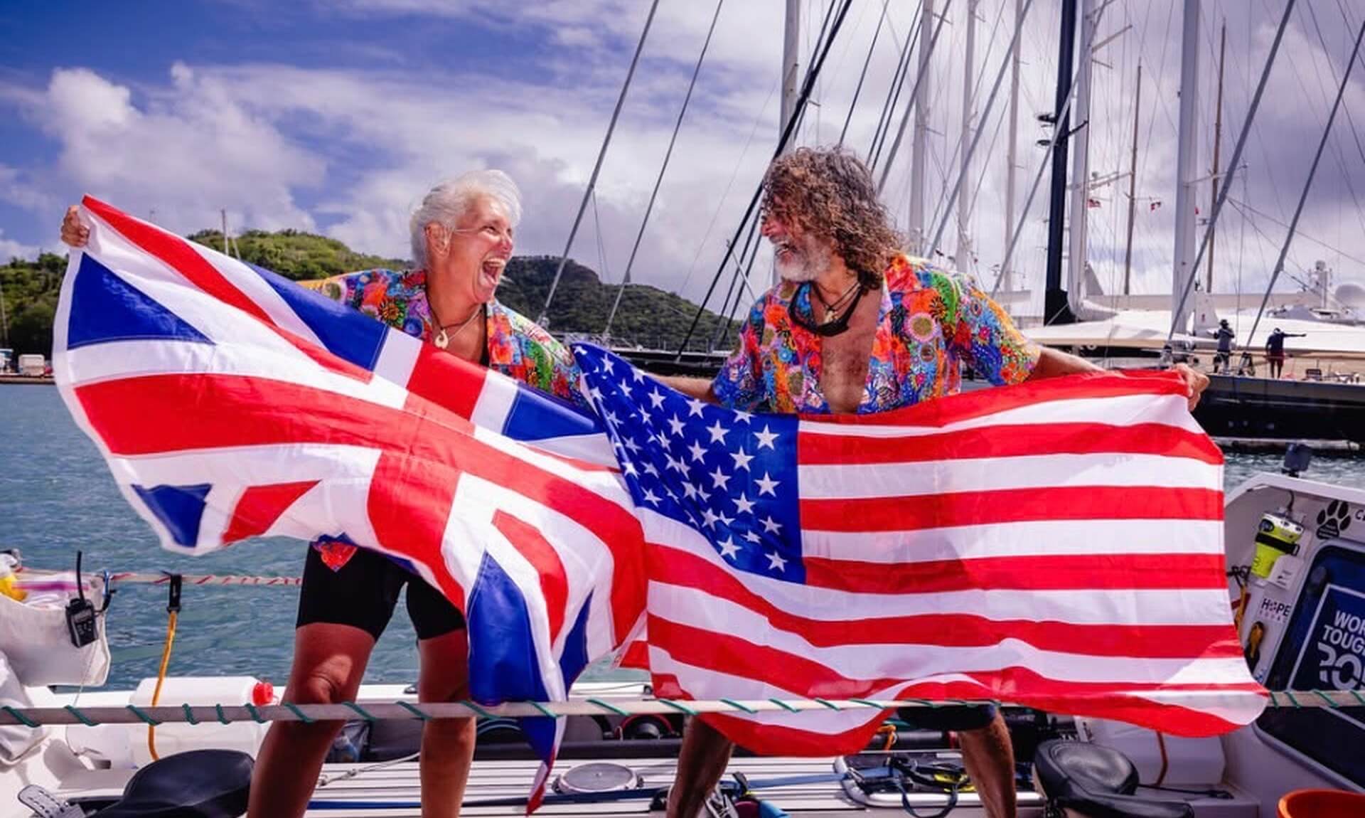 Dawn Smith and Paul Lore celebrating on their ocean rowing boat holding the Union flag and the Stars and Stripes