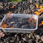 A disposable foil barbecue alight on stony ground with flames rising around it