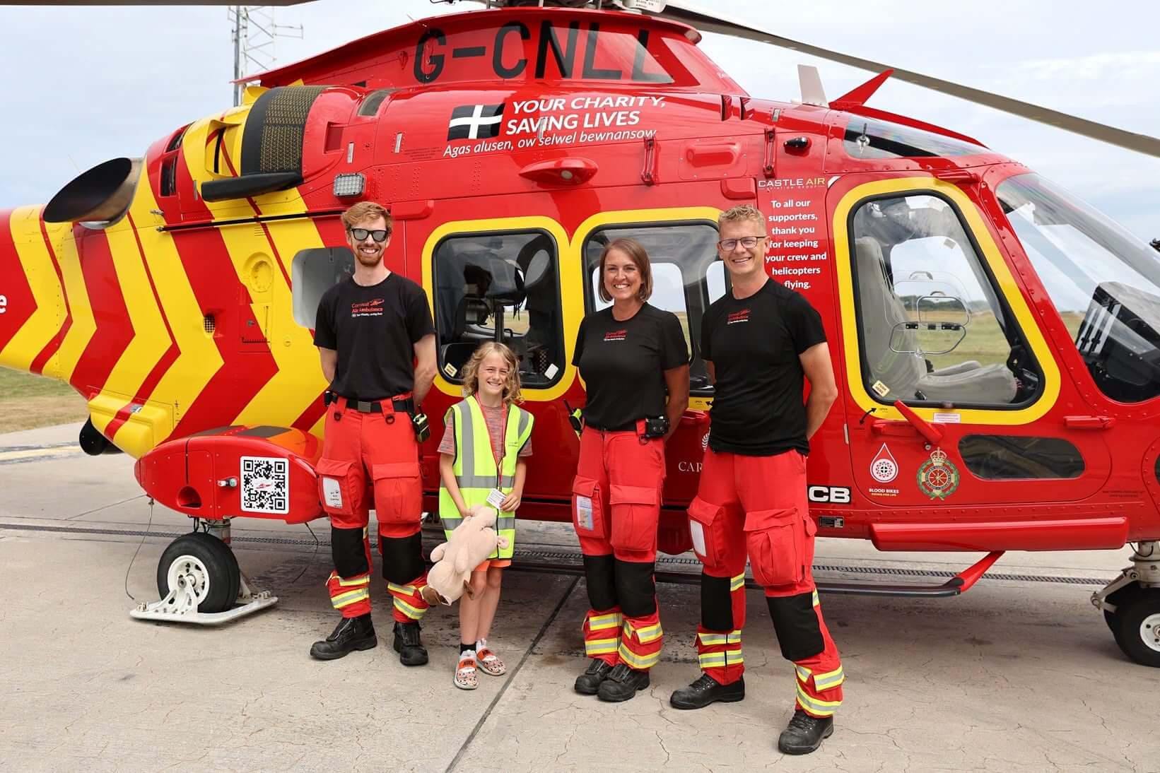 Freddie holding a teddy alongside three Cornwall Air Ambulance crew members by the helicopter