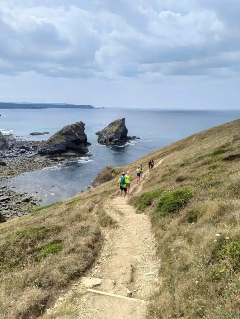 Runners on the coast path above sea stacks with the sea beyond
