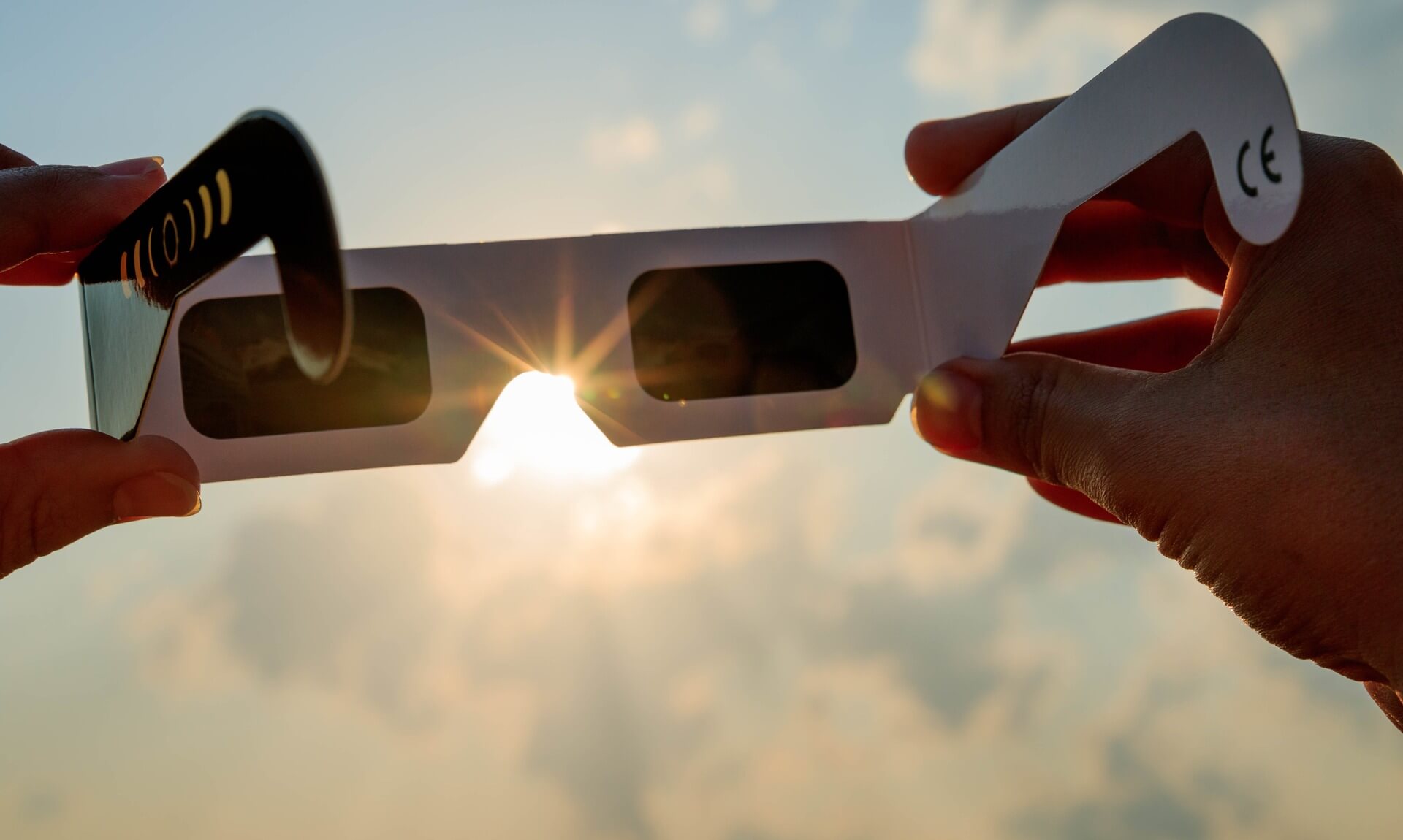 Hands holding CE-marked eclipse glasses up to a bright Sun