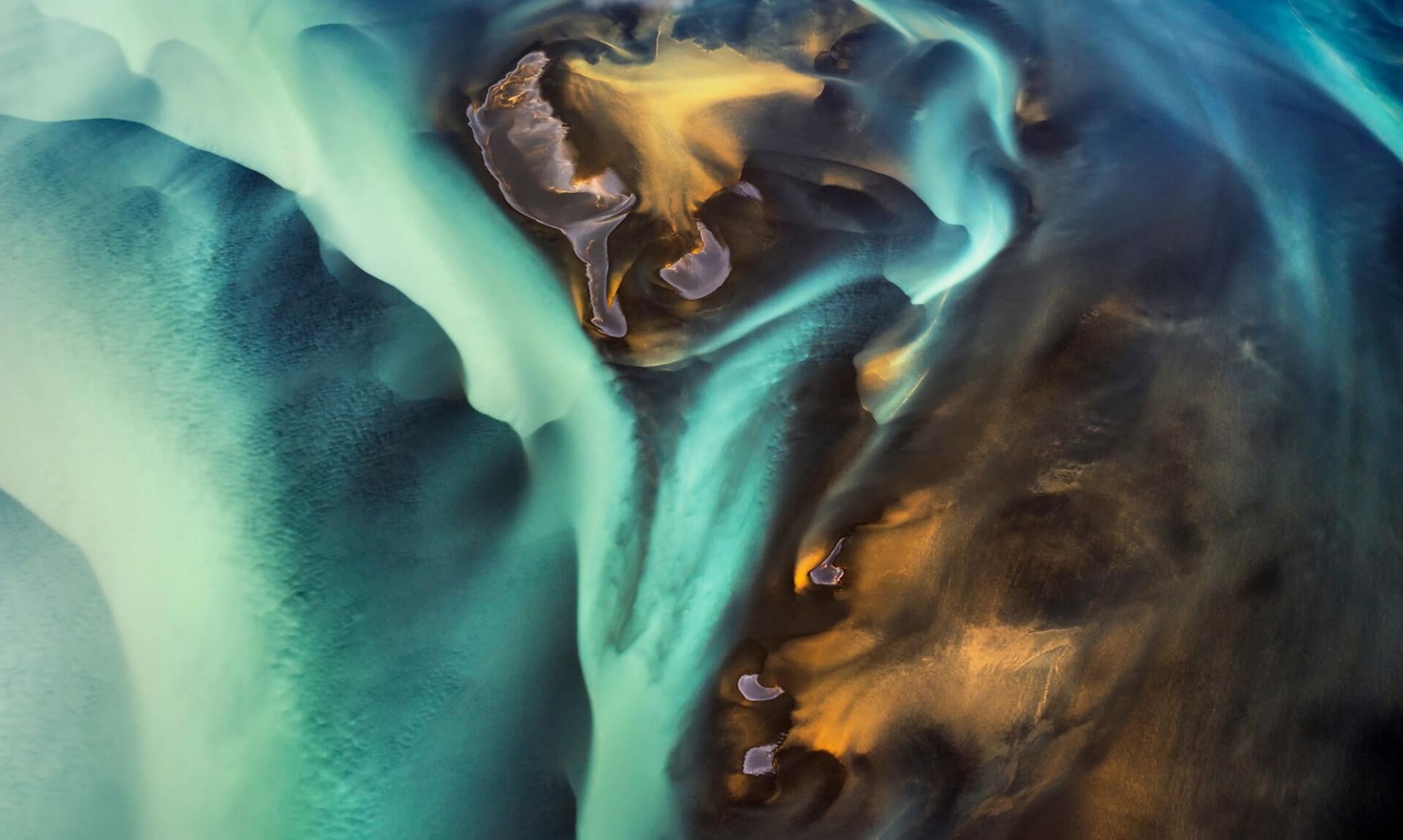 Aerial view of a glacial river in Iceland, turquoise and gold sediment swirling through dark volcanic sand