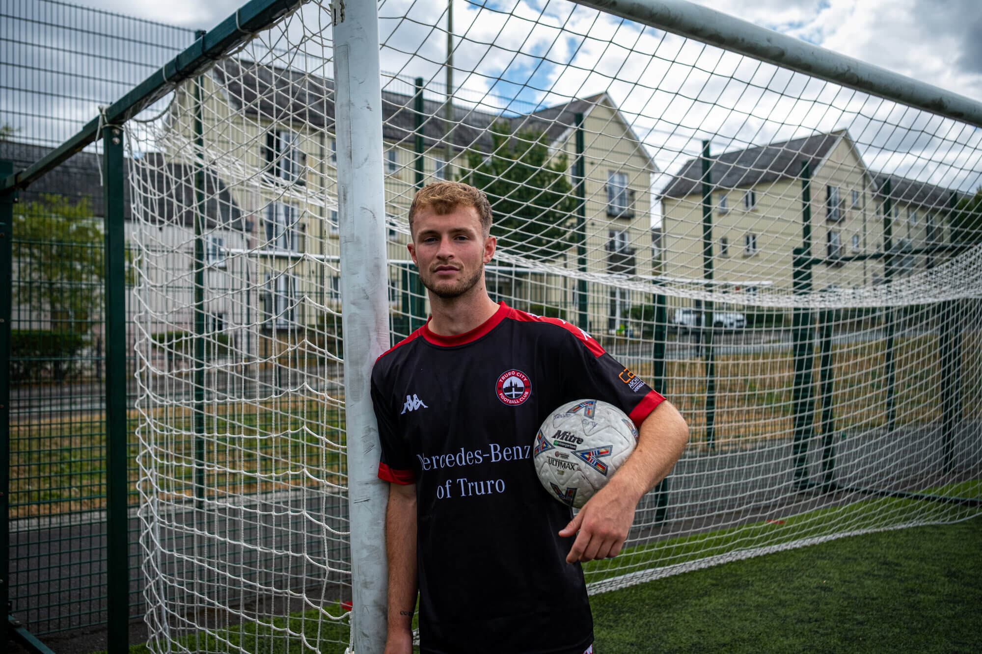 Max Kinsey leaning against a goalpost in Truro City training kit holding a football