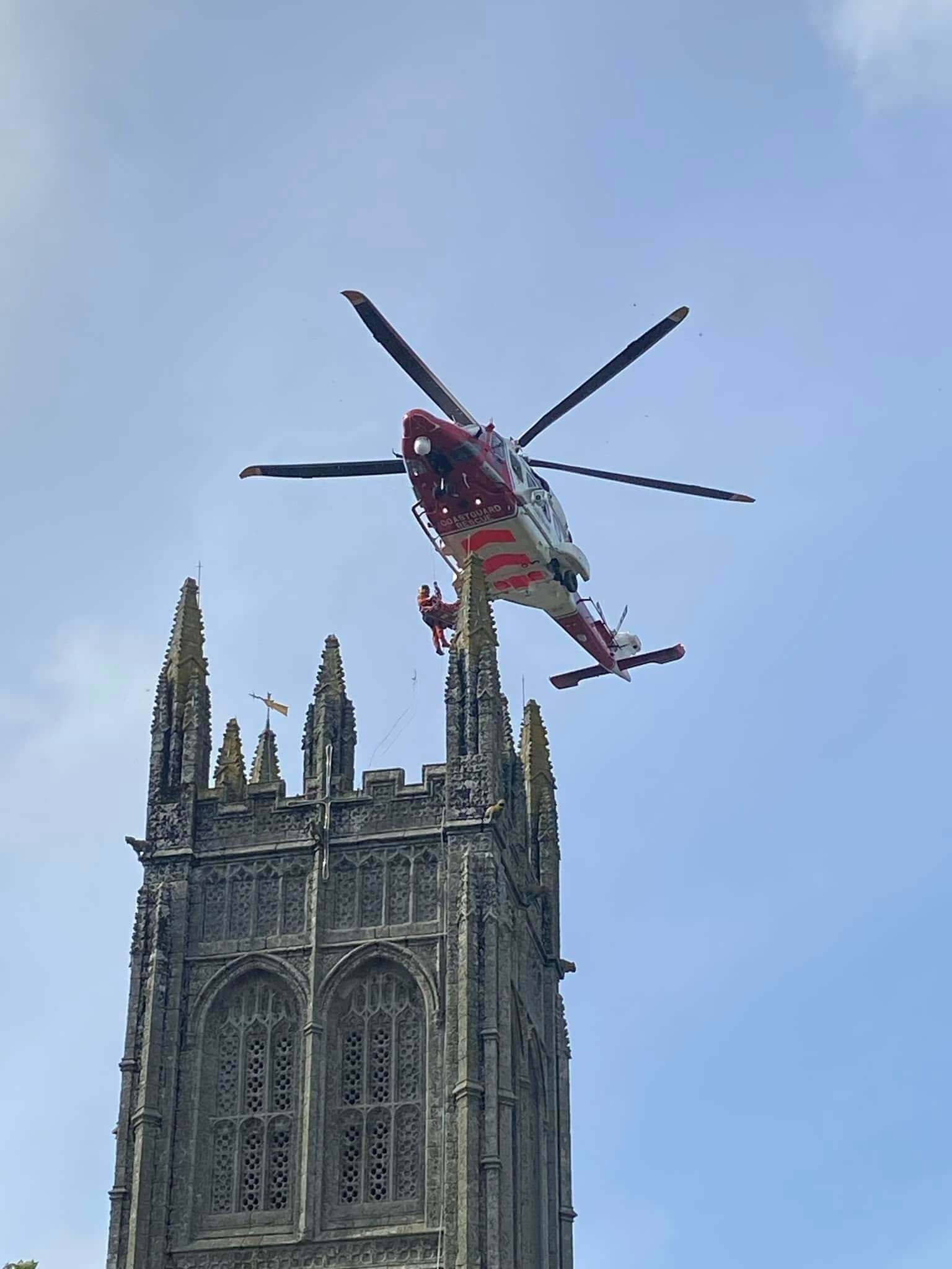 A Coastguard rescue helicopter hovering beside a church tower as a winchman is lowered onto the battlements