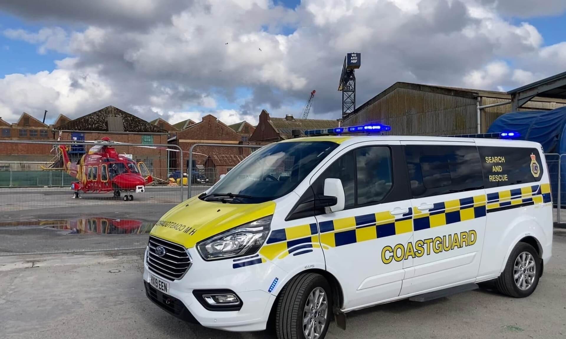 An HM Coastguard search and rescue vehicle parked in front of a red rescue helicopter at Falmouth docks