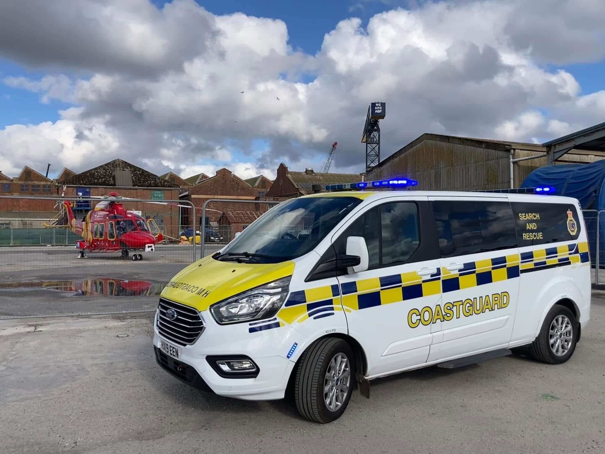 An HM Coastguard search and rescue vehicle parked in front of a red rescue helicopter at Falmouth docks