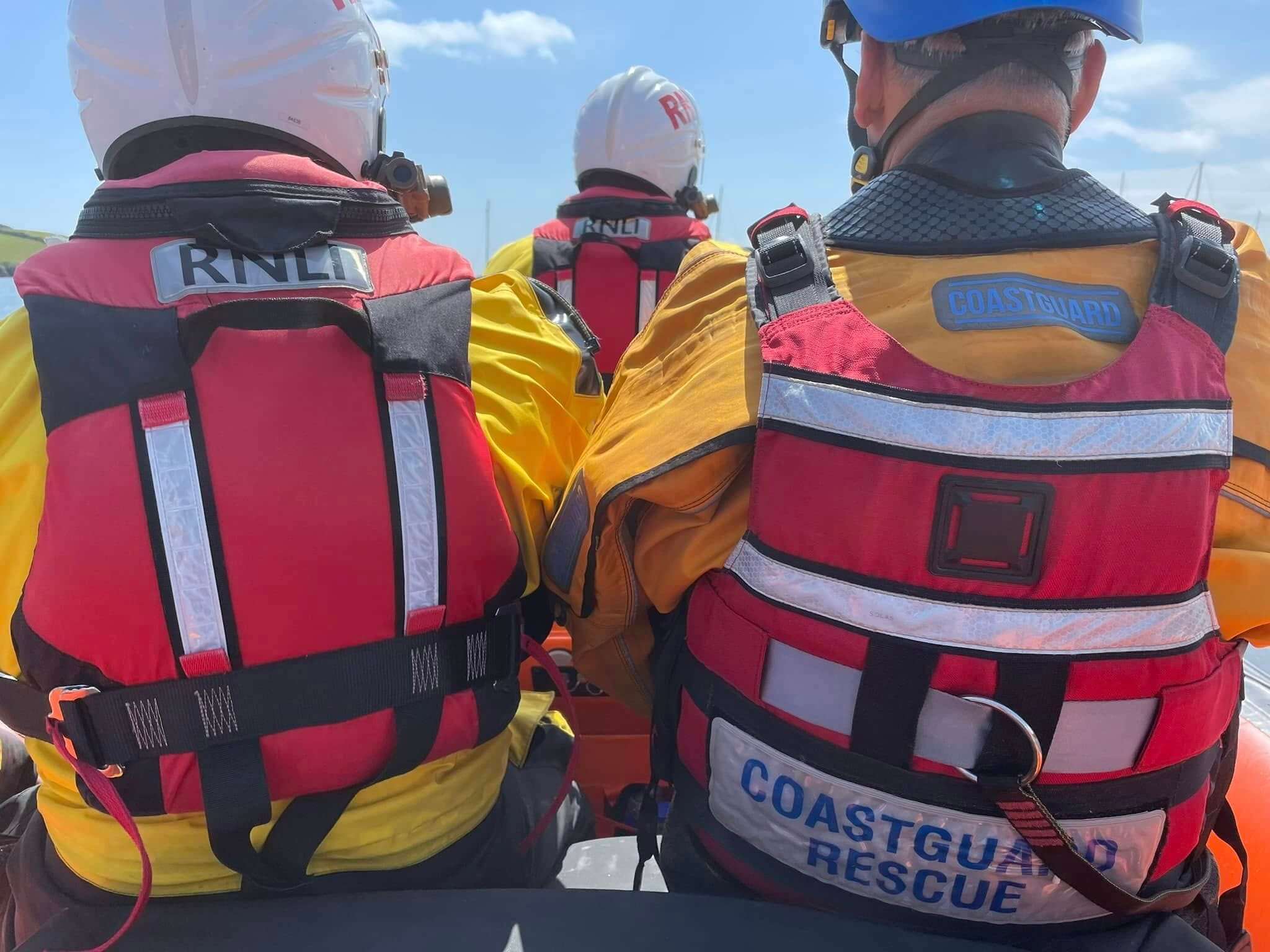RNLI lifeboat crew and a Coastguard rescue officer sitting on an inshore lifeboat on a sunny day