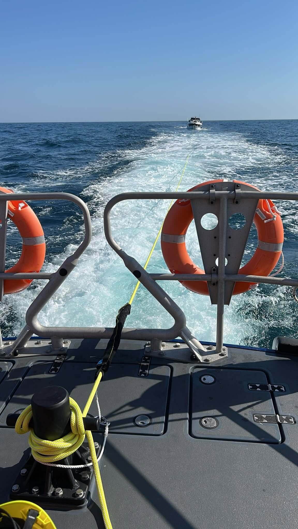 View from the stern of Falmouth's lifeboat with a yellow tow line leading to a cabin cruiser under tow on the horizon and orange lifebuoys on the rails