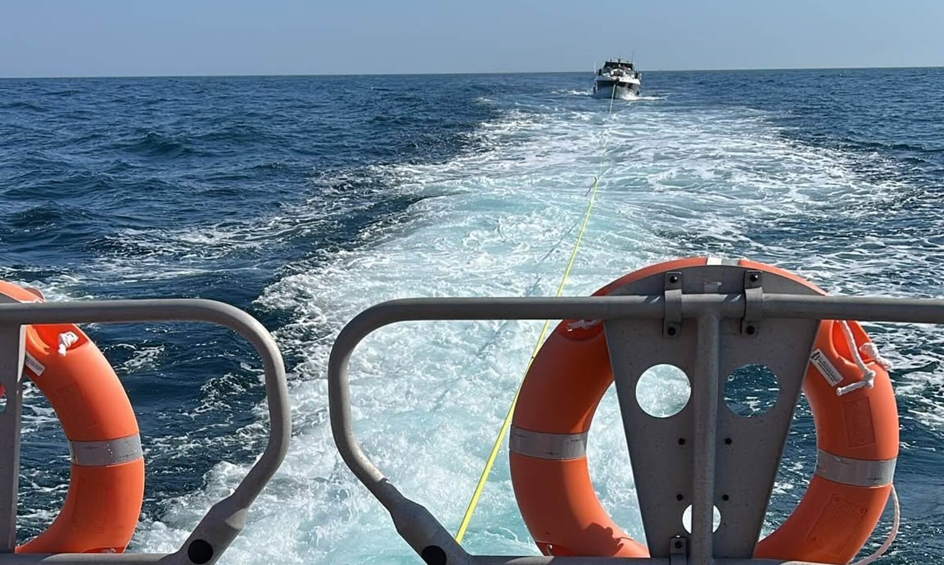 Yellow tow line running from the stern of Falmouth's lifeboat back to a cabin cruiser under tow on the horizon, framed by orange lifebuoys
