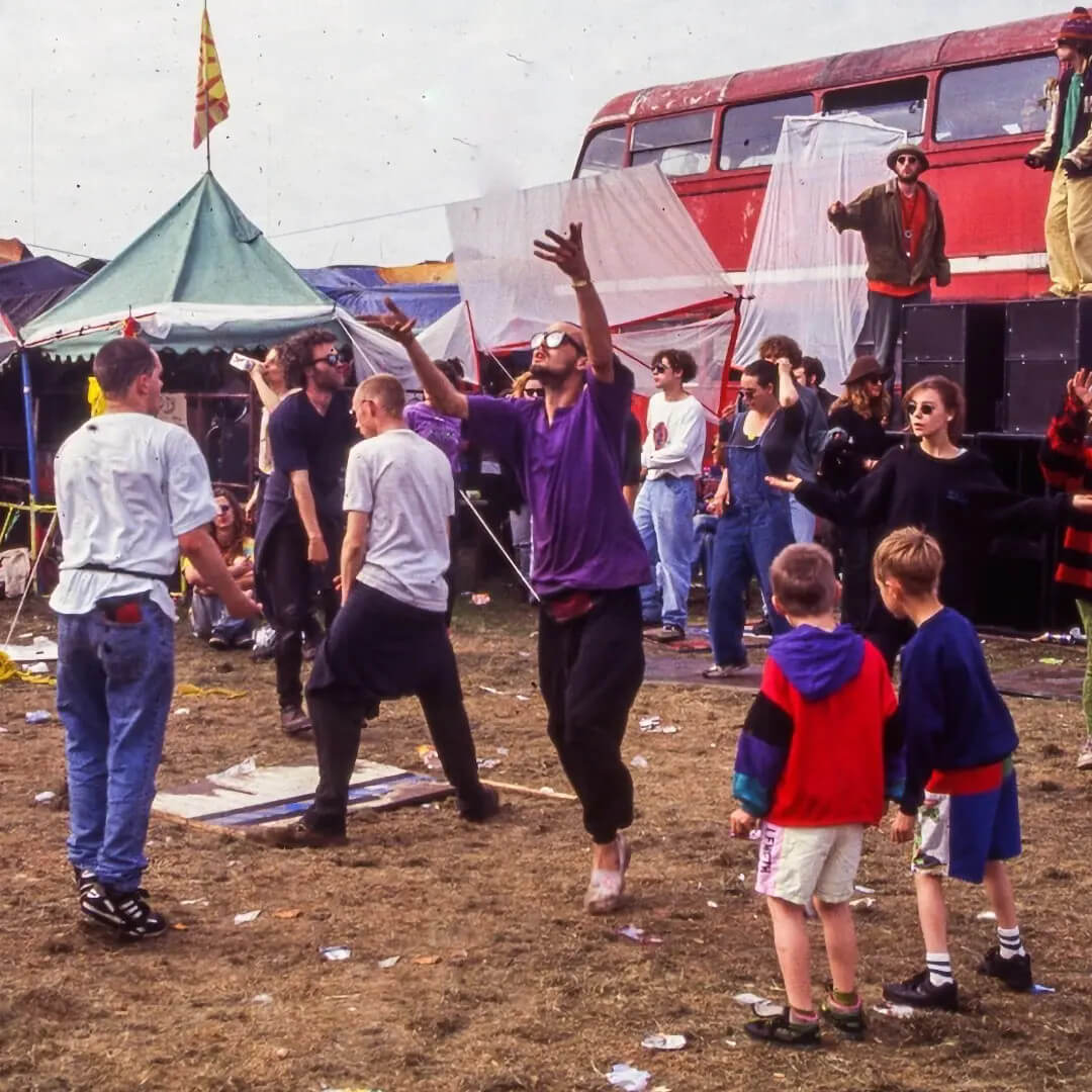 Crowd dancing at an outdoor free party in front of a red double-decker bus and speaker stacks